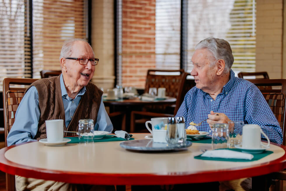 Two elderly men laughing while eating pie